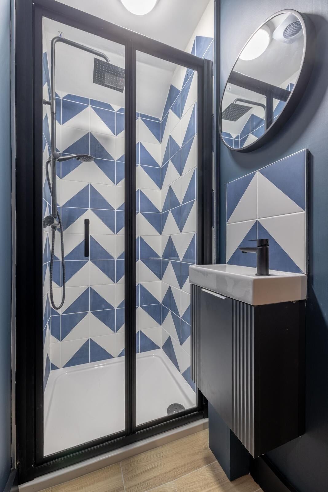 Une salle de bain moderne avec une douche, un lavabo avec un miroir et un revêtement mural en carreaux aux motifs géométriques.