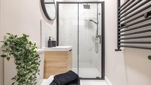 Un baño moderno con cabina de ducha de vidrio, tocador de madera, lavabo, espejo y planta en maceta.