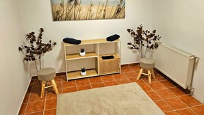 A room with a tiled floor, a beige rug, a wooden console table with shelves, two small stools, and a radiator.
