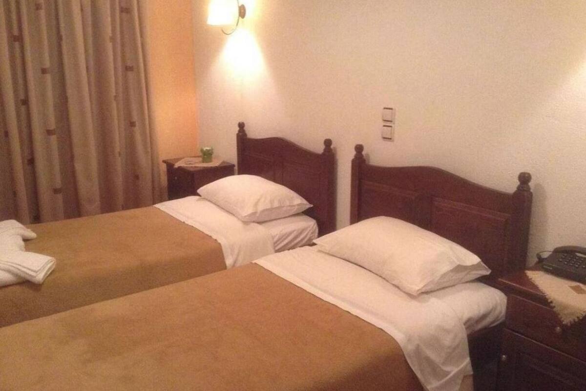 Una habitación de hotel con dos camas individuales, una mesita de noche con lámpara y una cortina.