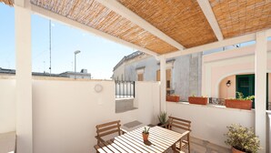 Eine überdachte Terrasse im Freien mit Tisch und Stühlen, Blumentöpfen und Blick auf die Stadtlandschaft.