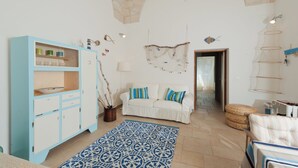 Ein Wohnzimmer mit einem weißen Sofa, einem blauen Teppich mit Muster, einer hellblauen Kommode und einer Steindecke.