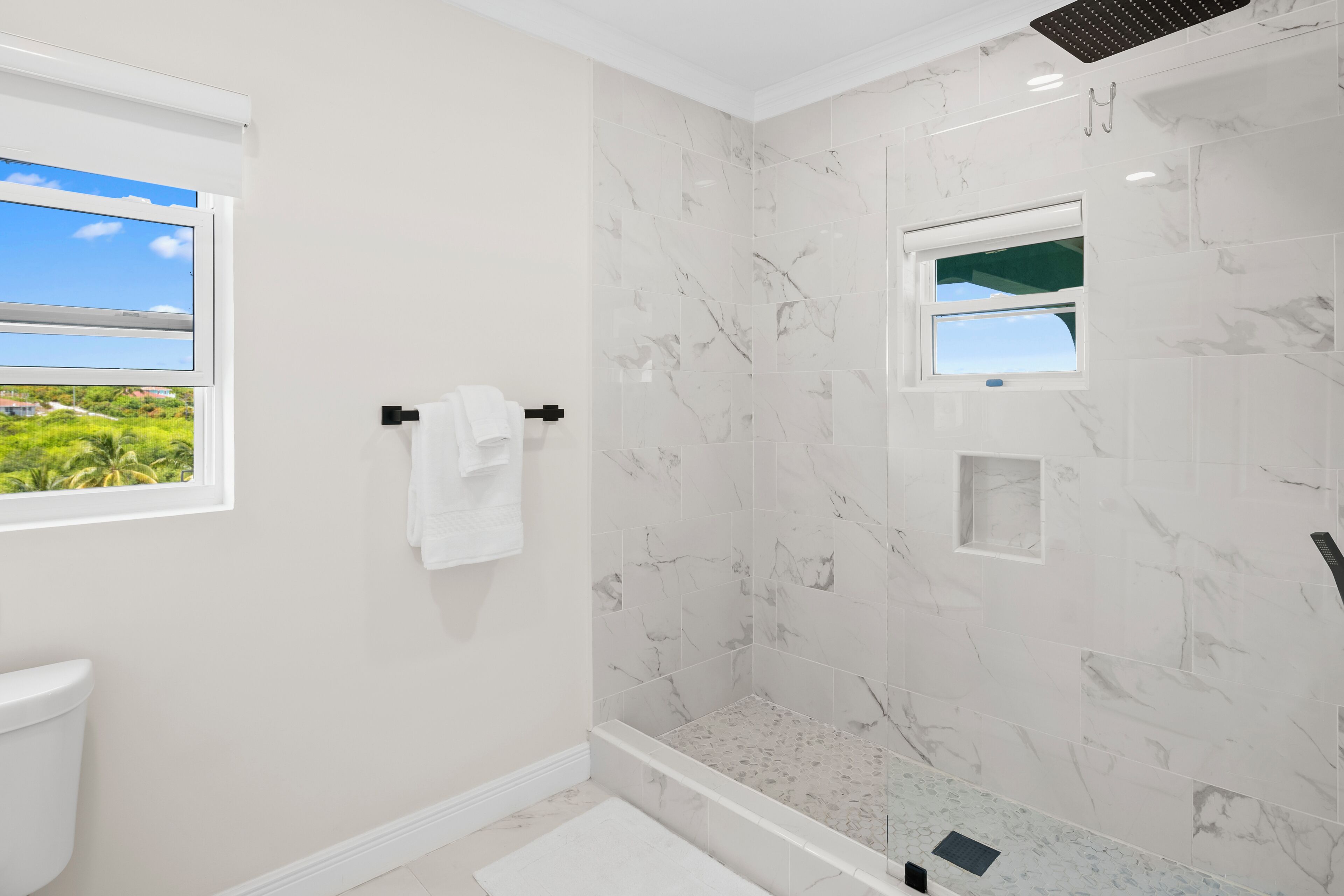 Ein modernes Badezimmer mit Dusche, Toilette und einem Fenster mit Blick auf Grünflächen.