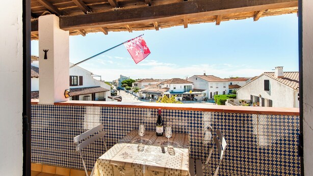 Un balcón con suelo de baldosas, una mesa con mantel y una bandera.