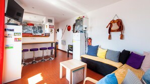 Un espacio habitable compacto con kitchenette, una zona de comedor con taburetes de bar, un sofá con varios cojines y una lámpara de pared.