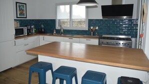 A modern kitchen with white cabinets, a wooden countertop, a gas stove, and blue stools. - Village house 5 mn walk from shops and 10 mn from beaches.  (Saint-Briac-sur-Mer)
