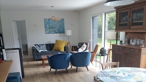 A spacious living area with a sofa, blue chairs, a dining table, and a kitchen area with cabinets. - Village house 5 mn walk from shops and 10 mn from beaches.  (Saint-Briac-sur-Mer)