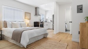 Une chambre moderne avec un grand lit, des tables de chevet et une vue sur la cuisine adjacente.