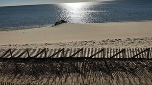 Uma praia com uma cerca de madeira ao primeiro plano e um céu claro.