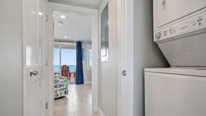 Corredor que dá para um quarto com vista, máquina de lavar e uma cadeira estampada.