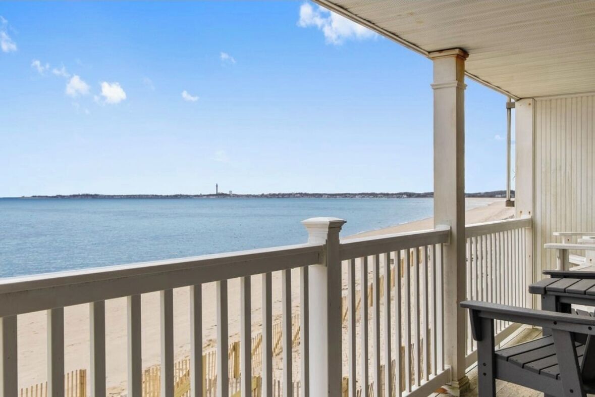 A beach view from a covered porch with white railings and a table.