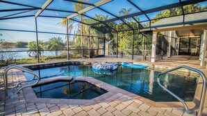 Piscina con jacuzzi, rodeada por un recinto de vidrio, con vistas a palmeras y un lago.
