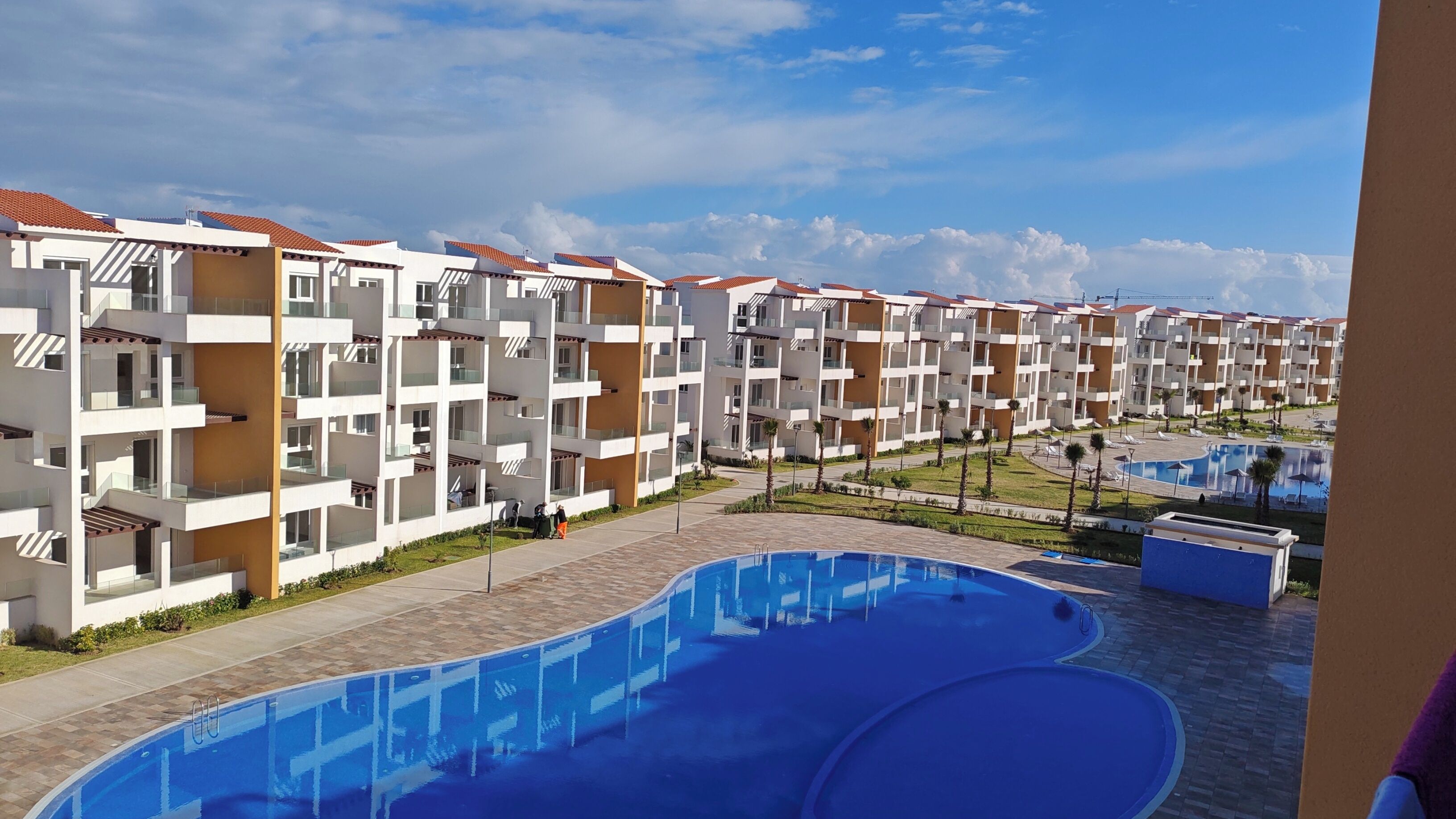Un hotel moderno con varios balcones, piscina y un jardín bien cuidado.