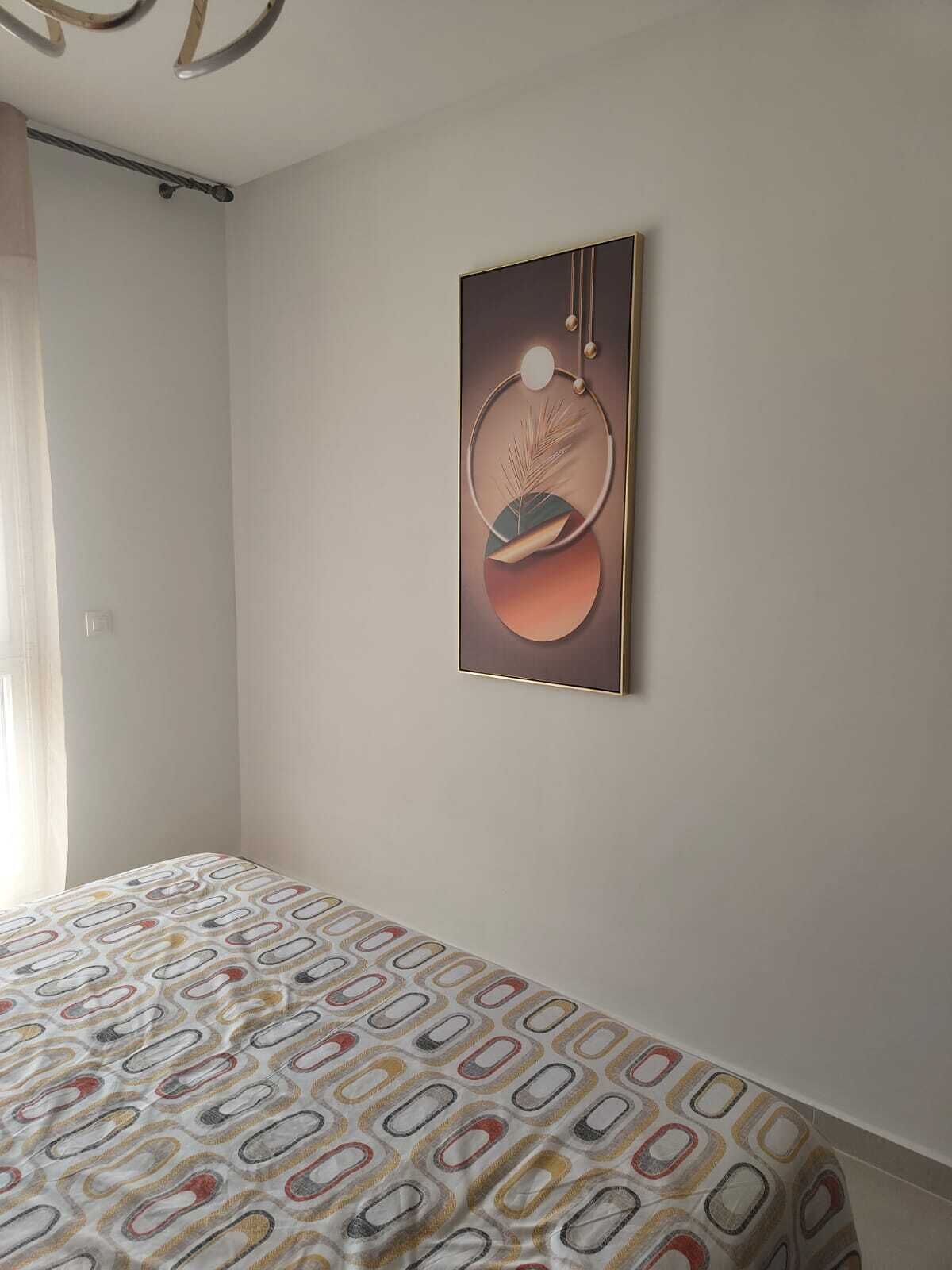 A bedroom with a bed, a wall-mounted abstract painting, and a window with curtains.