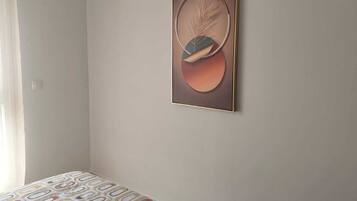 A bedroom with a bed, a wall-mounted abstract painting, and a window with curtains.