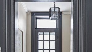 Una porta de fusta fosca amb finestral de motius de graella, una banca de fusta i un moqueta amb dibuixos de punt de paviment.