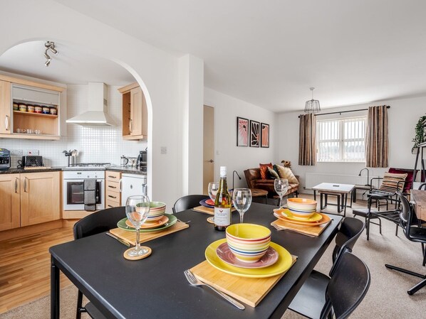 A modern kitchen with wooden cabinets, a built-in oven, and a dining area with a black table set for four. - The Point, 2 Bed Flat, Parking - Pass the Keys (Liverpool)
