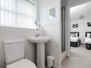 A modern bathroom with a toilet, sink, and shower. There is a trash bin and a mirror above the sink. The room leads to a bedroom with two beds. - The Point, 2 Bed Flat, Parking - Pass the Keys (Liverpool)