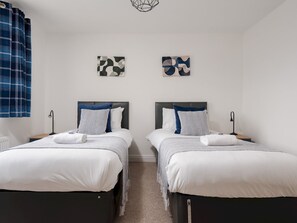 A double room with two beds, each with a headboard, white bedding, and a blue and white patterned pillow. There are two wall-mounted artworks, a window with blue curtains, and a ceiling light fixture. - The Point, 2 Bed Flat, Parking - Pass the Keys (Liverpool)