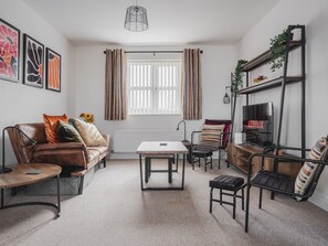 A modern living room with a brown leather sofa, a white coffee table, a TV on a wooden stand, and a bookshelf with plants. - The Point, 2 Bed Flat, Parking - Pass the Keys (Liverpool)