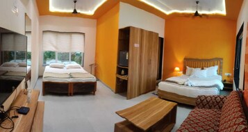 Quarto de hotel com duas camas, um guarda-roupa de madeira, um sofá vermelho com padrão e uma mesa de madeira.