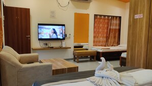 A hotel room with a television, a sofa, a wooden table, a bed, and a shower curtain. - Supriti's Farmington Splash Resort (Karjat)