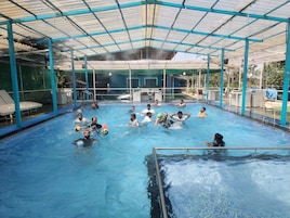An indoor swimming pool with a covered roof, surrounded by lounge chairs and a poolside area.