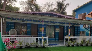 A blue building with a white balcony, surrounded by green grass and potted plants. - Supriti's Farmington Splash Resort (Karjat)