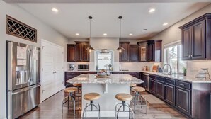 A modern kitchen with a large island, bar stools, stainless steel appliances, and dark wood cabinets. - 5400sqft 6BR 5.5BA Theater, Office, Game Room // 10min to DIA & Downtown (Denver)