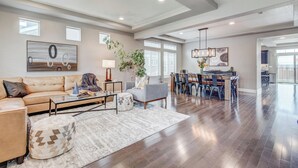 A spacious living room with a large sofa, a coffee table, and a dining area with a kitchen in the background. - 5400sqft 6BR 5.5BA Theater, Office, Game Room // 10min to DIA & Downtown (Denver)