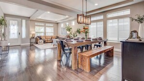 A spacious living room with a wooden dining table, a sofa, and a bench. - 5400sqft 6BR 5.5BA Theater, Office, Game Room // 10min to DIA & Downtown (Denver)