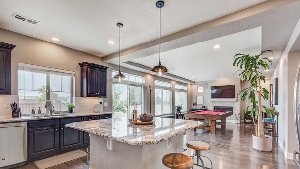 A spacious kitchen with dark cabinets, a large island with stools, pendant lighting, and a pool table in the adjacent living area. - 5400sqft 6BR 5.5BA Theater, Office, Game Room // 10min to DIA & Downtown (Denver)