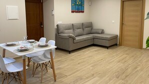 Un saló modern amb taula de menjador, cadires blanques, un sofà modular gris i un terra de fusta.