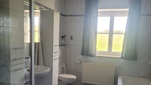 A bathroom with a glass shower enclosure, a toilet, a sink, a bathtub, and a window with curtains. - Vacation apartments Meyer, between Nuremberg and Ansbach A6/B14, near Playmobil Fun Park (Heilsbronn)