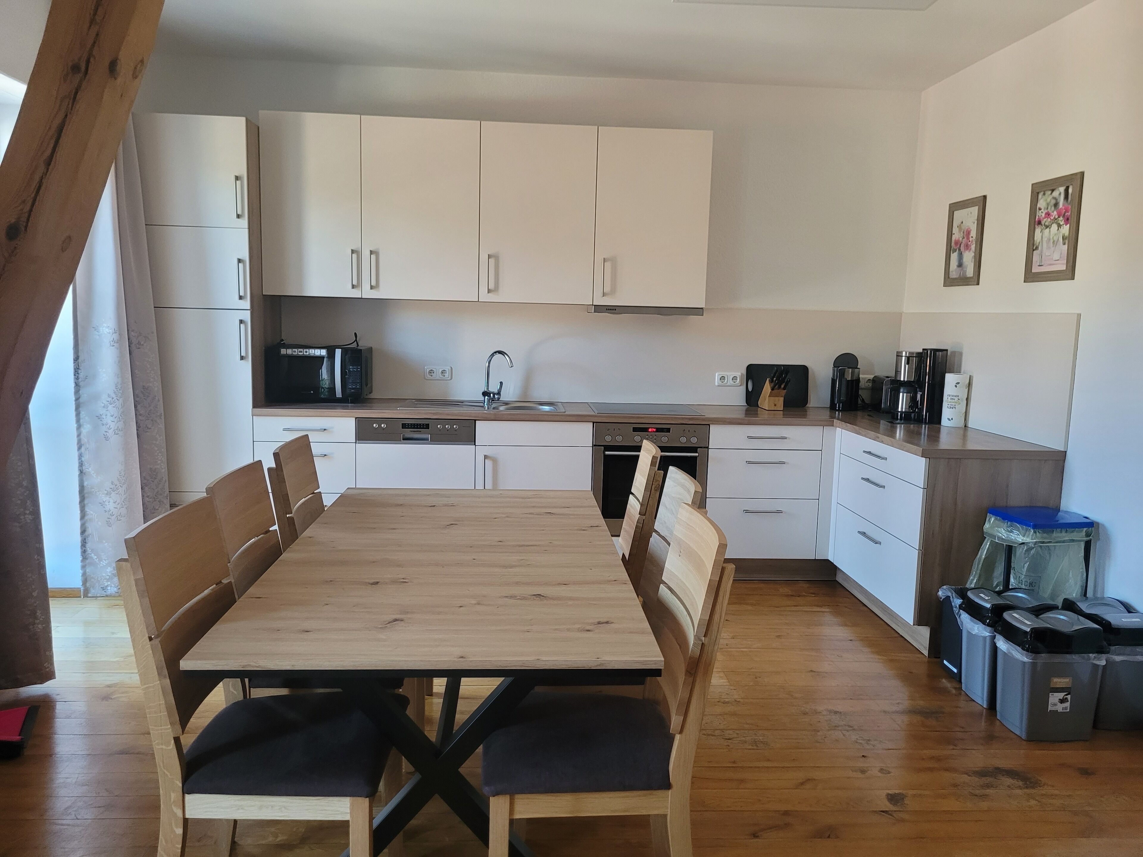 A modern kitchen with white cabinets, a wooden dining table, and a built-in oven.