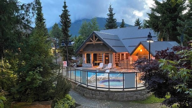 Un lodge con piscina, vialetto in pietra e sfondo boscoso.