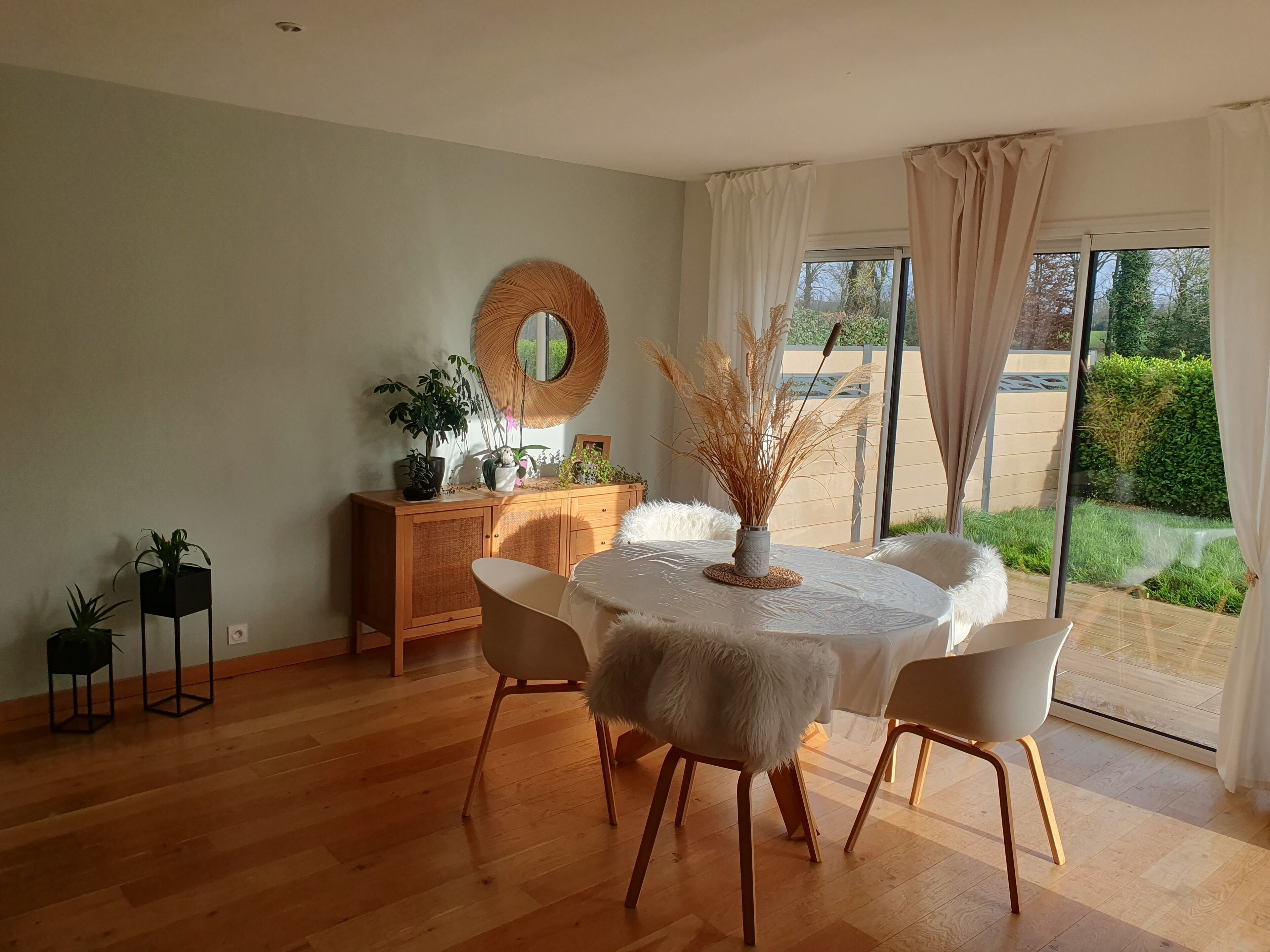 Een eethoek met een ronde tafel, witte stoelen en een houten kast met planten.