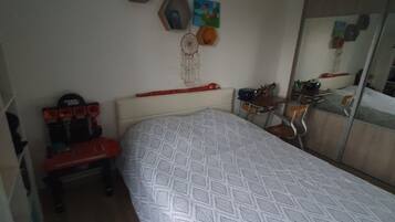 Une chambre à coucher avec une couvre-lit à motifs, un bureau avec une chaise, une commode et des décorations murales, notamment un attrape-rêves et des tableaux encadrés.