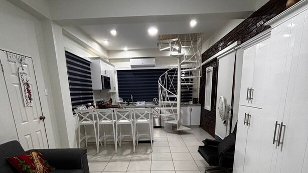 A modern kitchen with white cabinets, a dining area with white chairs, and a black sofa with a red cushion. - Charming 2-bedroom apartment with WiFi, AC in pleasant Westmoorings (Diego Martin Regional Corporation)