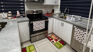A modern kitchen with white cabinets, a microwave, a stove, and a sink. - Charming 2-bedroom apartment with WiFi, AC in pleasant Westmoorings (Diego Martin Regional Corporation)