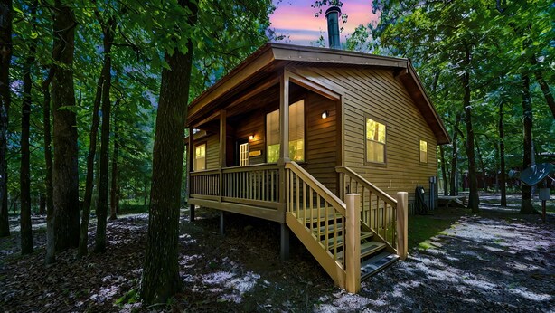 A wooden cabin with a porch and stairs, surrounded by trees.