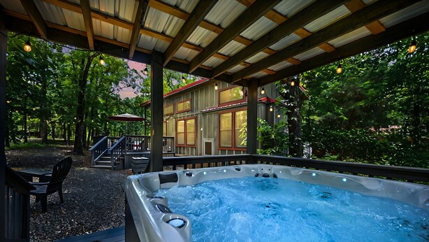 Un bain à remous sous une pergola en bois, avec vue sur une maison et des arbres.