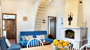 A living room with a blue sofa, wooden dining table, and a bowl of lemons. - COZY VILLA ZOI (Tzitzifes)