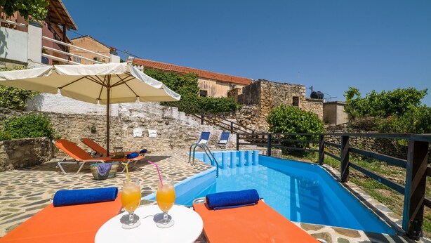A poolside area with lounge chairs, umbrellas, and a table with drinks. - COZY VILLA ZOI (Tzitzifes)