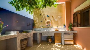 A compact kitchen with a marble countertop, a sink, and a built-in oven. There are potted plants and decorative items on the counter. - COZY VILLA ZOI (Tzitzifes)