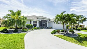 A modern two-story house with a curved driveway, surrounded by well-maintained lawns and palm trees.