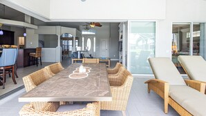 A spacious patio with a dining table surrounded by wicker chairs, a ceiling fan, and a view of the interior through glass doors.