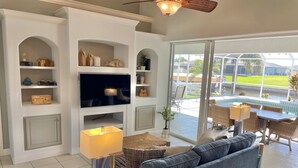 A living room with a large TV, a sofa, and a dining area with wicker furniture.