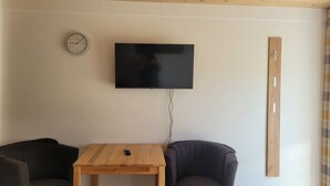 A living room with a flat-screen TV mounted on the wall, a wooden table, two armchairs, and a clock on the wall. - Vacation apartments Meyer, between Nuremberg and Ansbach A6/B14, near Playmobil Fun Park (Heilsbronn)