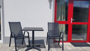 An outdoor patio with two chairs and a table, a red door, and a white wall. - Vacation apartments Meyer, between Nuremberg and Ansbach A6/B14, near Playmobil Fun Park (Heilsbronn)